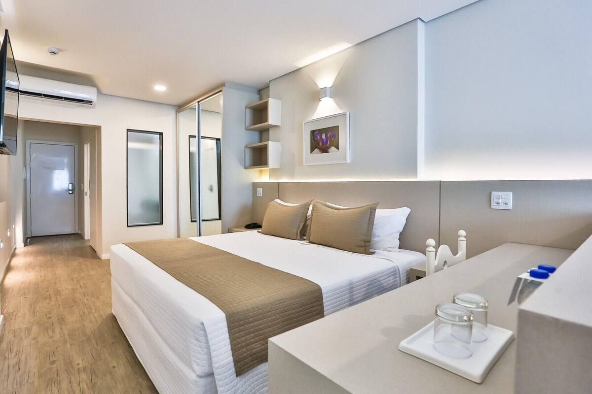 A hotel room with a bed, bedside table, and a mirror.