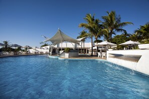 Piscina con sillones blancos y sombrillas, rodeada de palmeras.
