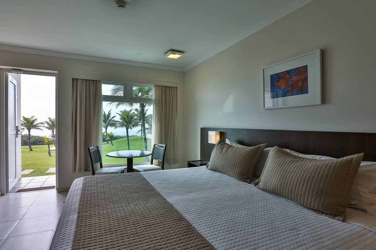 A hotel room with a large bed, a dining table with chairs, a view of the outdoors, and a framed picture on the wall.