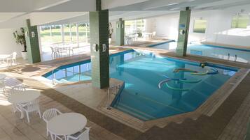 Una piscina interior con agua cristalina, rodeada de sillas y mesas blancas, y grandes ventanales con vistas al exterior.