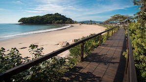 Una passerella in legno lungo una spiaggia, con vista sull'oceano e una collina boscosa all'orizzonte.