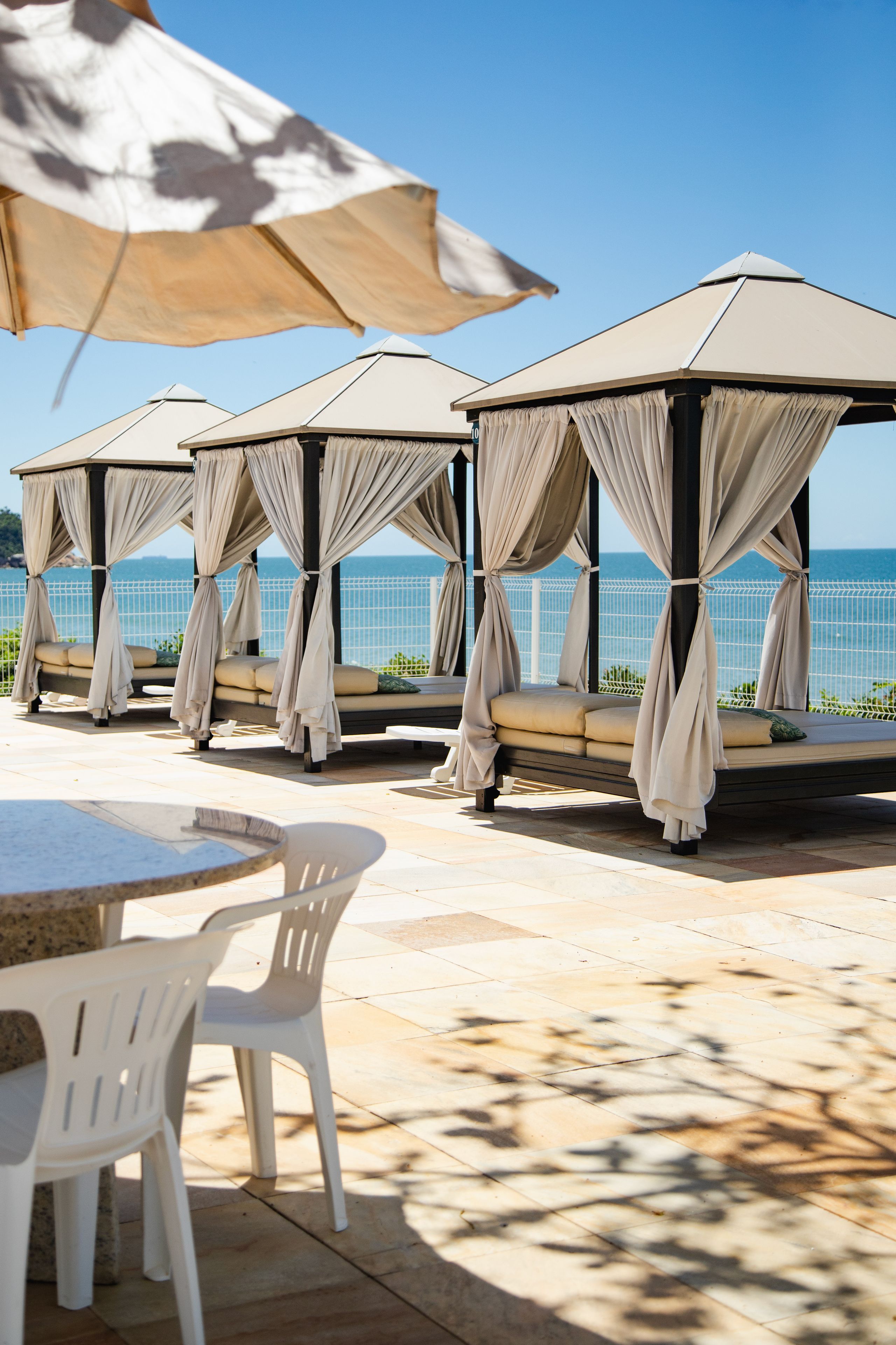 Um alpendre à beira-mar com quatro áreas de estar cobertas, uma mesa e cadeiras.