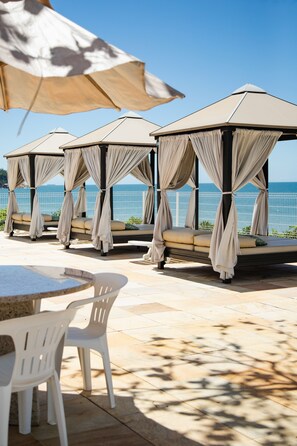 Un patio frente al mar con cuatro zonas de estar cubiertas, una mesa y sillas.