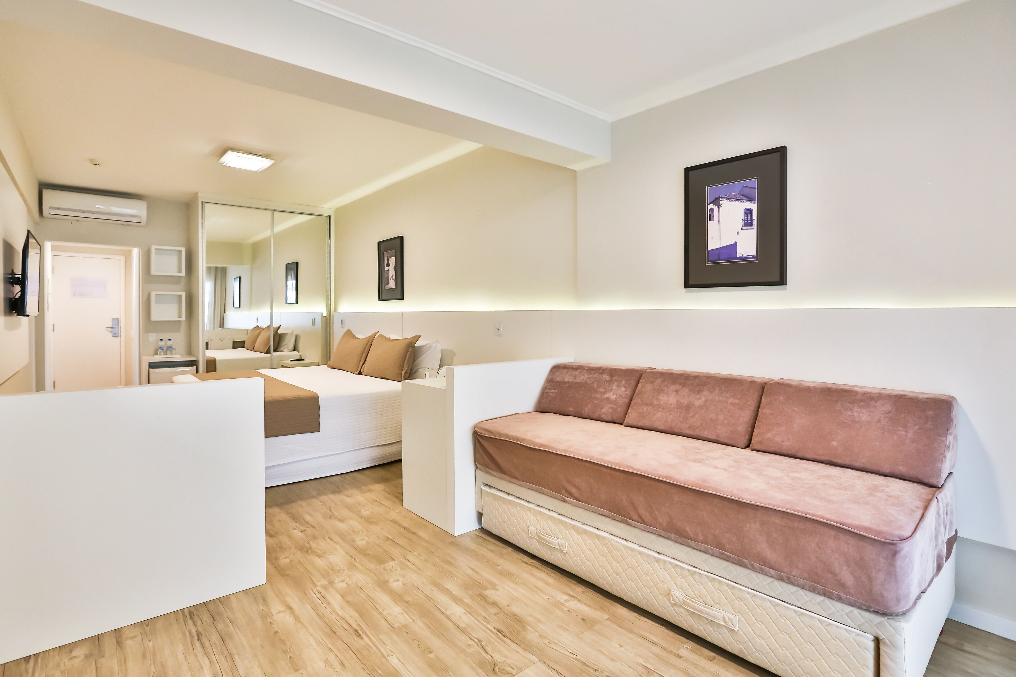 A modern bedroom with a large bed, a pink sofa, and a mirror.