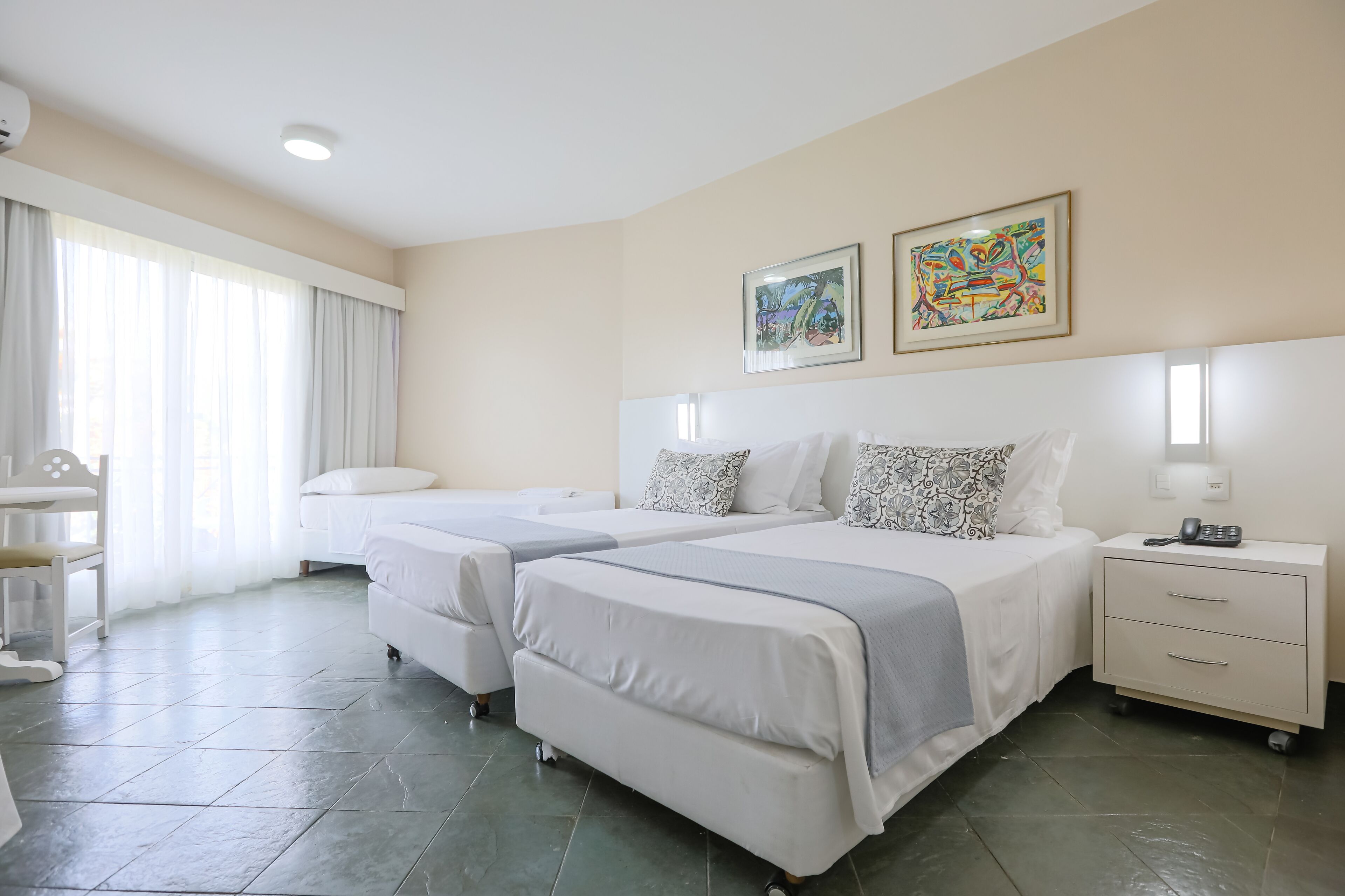 Habitación de hotel con dos camas, un escritorio, una silla y obras de arte en las paredes.