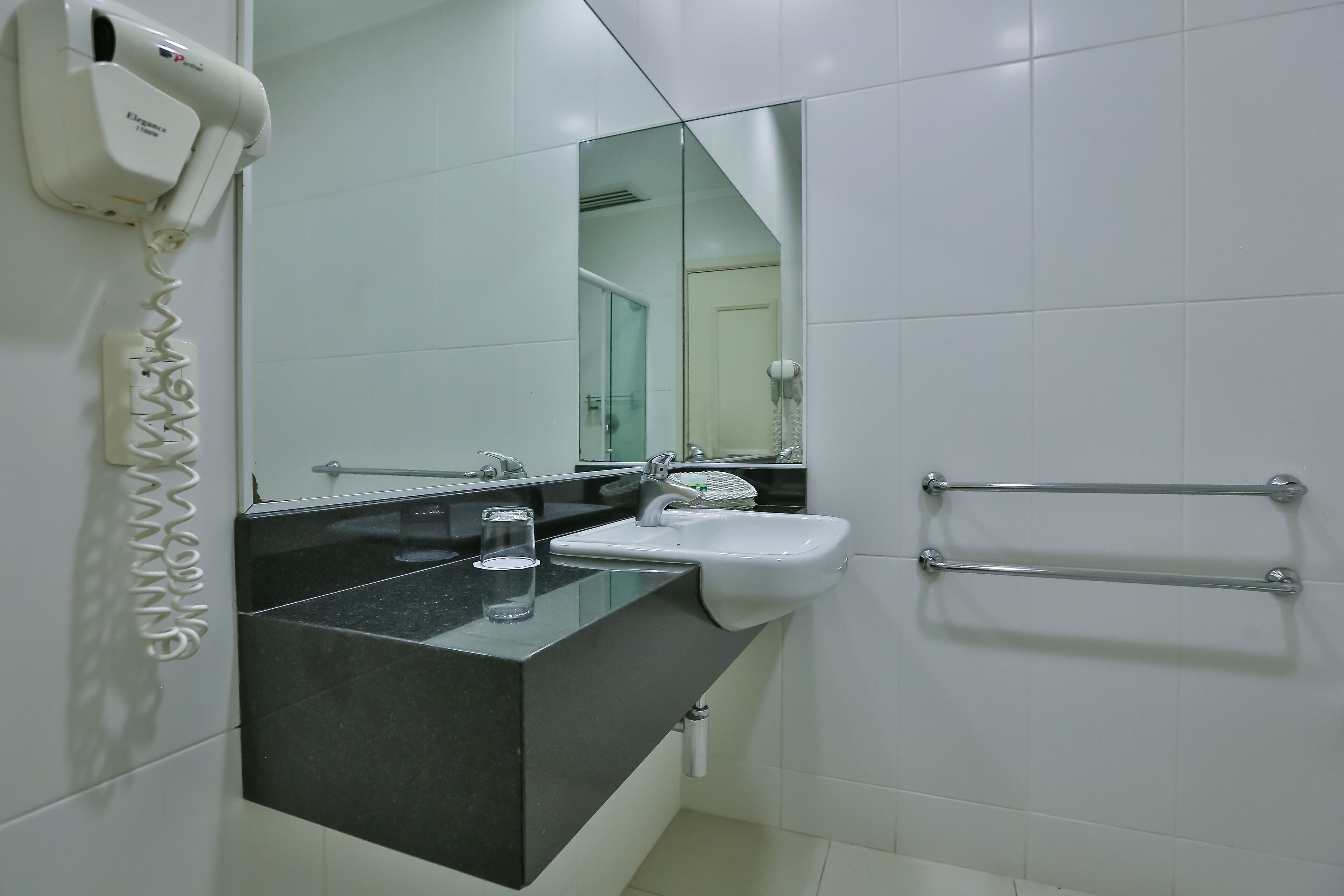 Un baño con encimera negra, lavamanos blanco y secador de manos.
