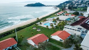 Vista aerea di una località balneare con spiaggia, piscina e diversi edifici con tetti in tegole rosse.