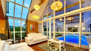 A modern interior with large windows, a white sofa, a small table, and a pool visible through the glass. - House / Villa - Plouescat (Plouescat)