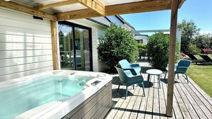 Een hottub op een houten terras, met een glazen deur naar een huis, omringd door tuinmeubels.