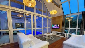 A modern living room with a large TV, white sofas, and a pool visible through the glass doors. - House / Villa - Plouescat (Plouescat)