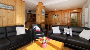 Un salón comedor con paneles de madera, dos sofás negros, una mesa de centro con flores y una chimenea.