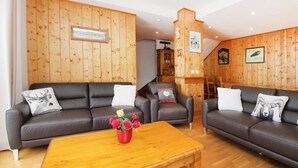 Una sala de estar acogedora con dos sofás de cuero oscuro, una mesa de centro de madera y un jarrón rojo con flores.