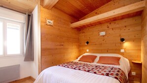 Dormitorio con paneles de madera, una cama, dos luces fijadas a la pared y un ventanal con cortina.