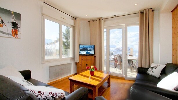 Una sala de estar con un sofá, una mesa de centro con flores, un televisor y un ventanal corredizo que da a un área exterior.