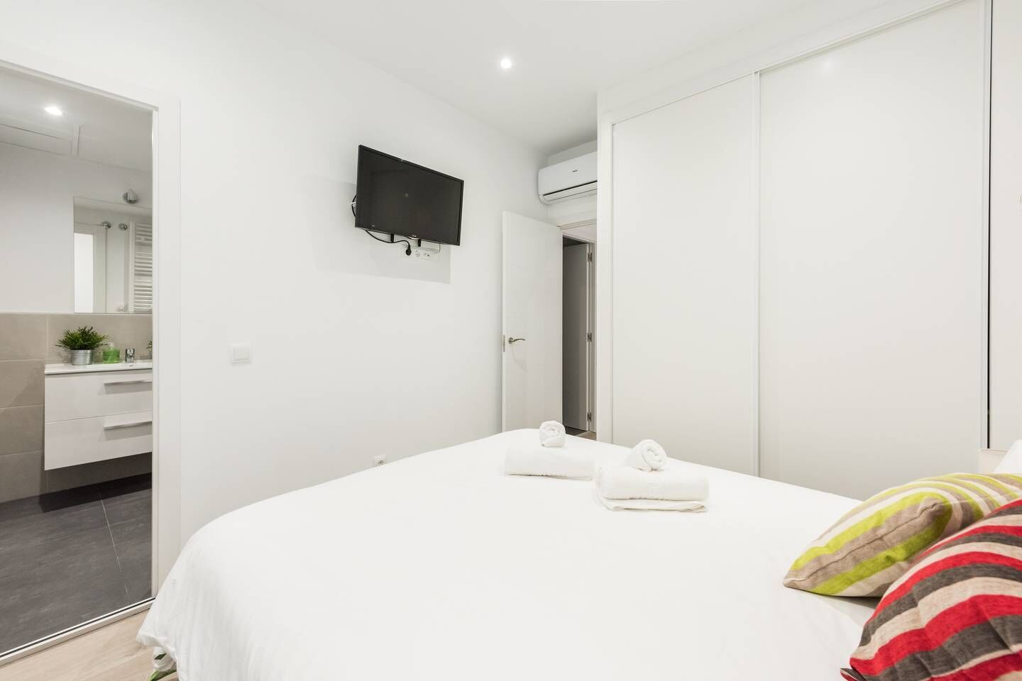 Une chambre à coucher moderne avec un lit, un téléviseur fixé au mur et un dressing.