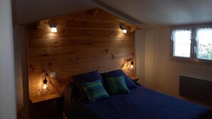 Un dormitorio con cabecera de madera, cama con ropa de cama azul, dos lámparas de noche y una ventana con cortinas.