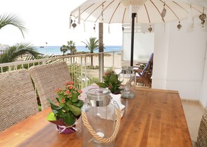 A wooden table with glass candle holders and a potted plant, set on a balcony with a view of the sea.