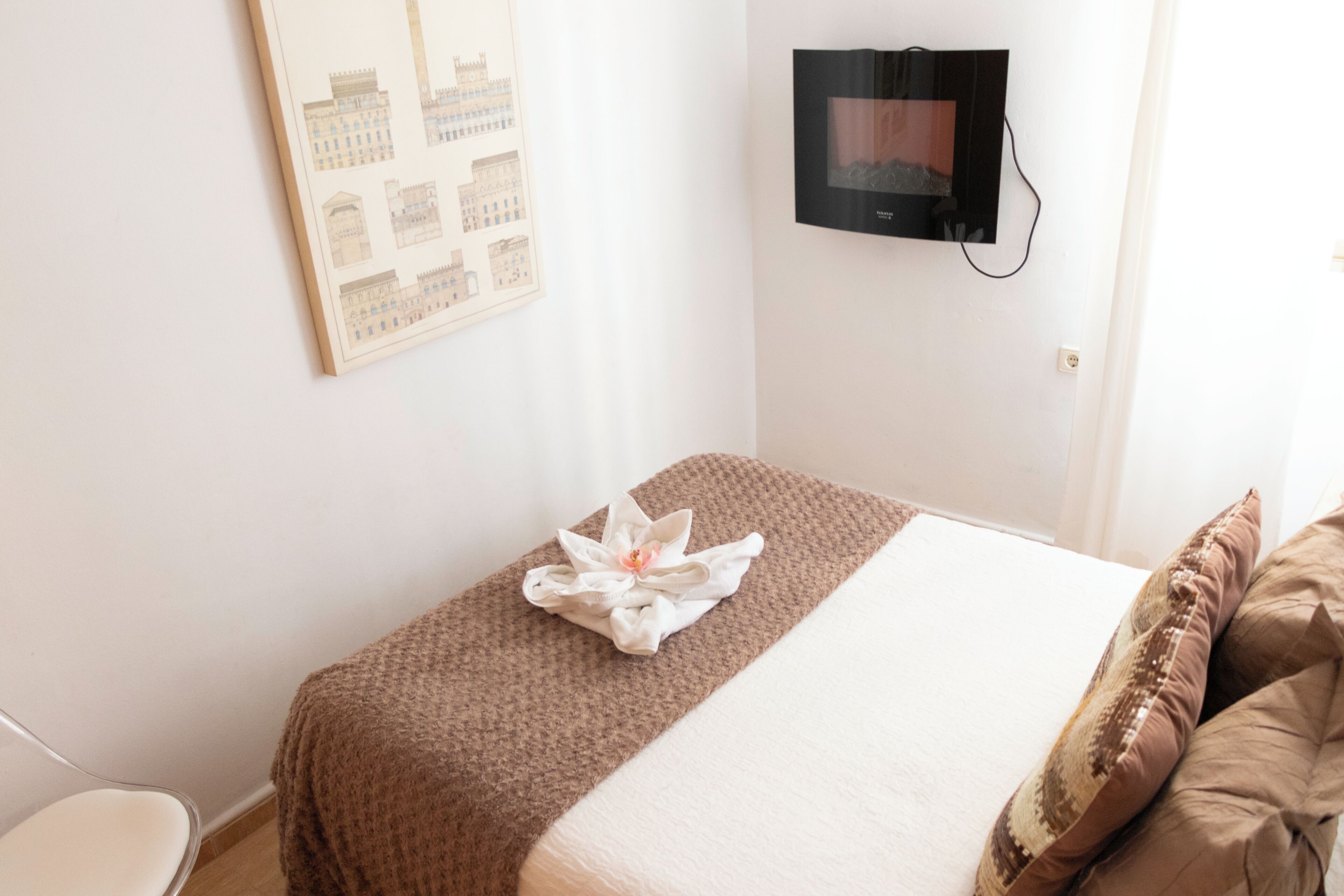 A hotel room with a bed, a television mounted on the wall, and a framed architectural drawing on the wall.