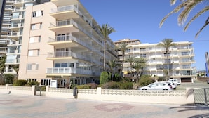 A multi-story residential building with balconies, a gated entrance, and a parking area with cars. - Family-friendly apartment 20 m from Arenal Beach, Calpe (CALPE)