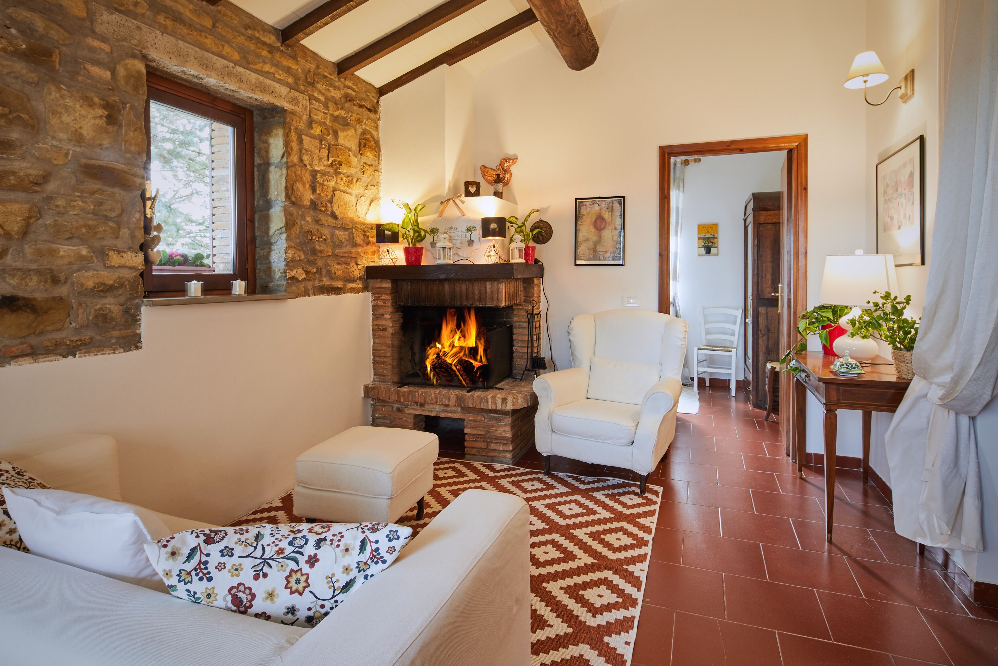 A cozy living room with a fireplace, stone walls, and a patterned rug.