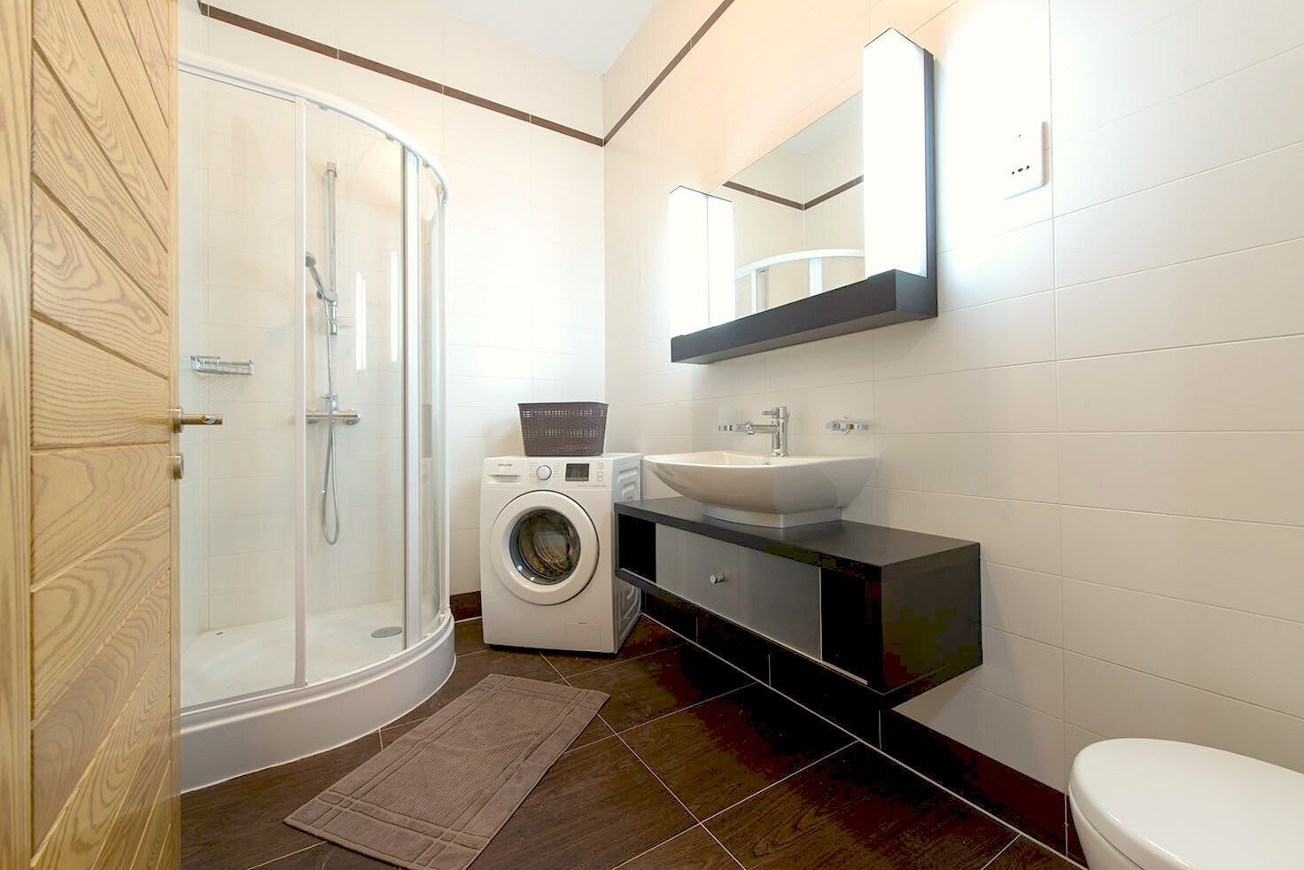 Une salle de bain moderne avec une douche à parois de verre, un lave-linge, un évier et des toilettes.