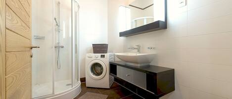 Une salle de bain moderne avec une douche à parois de verre, un lave-linge, un évier et des toilettes.