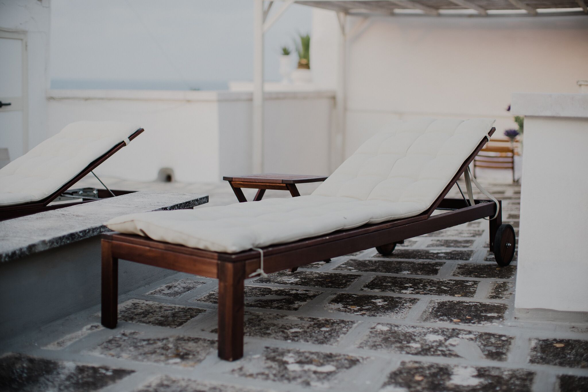 Eine Reihe von Holzliegestühlen mit weißen Kissen auf einer gefliesten Terrasse.