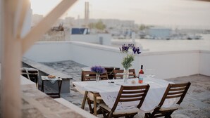 Una mesa de comedor en una terraza en la azotea, con vista al mar y edificios.