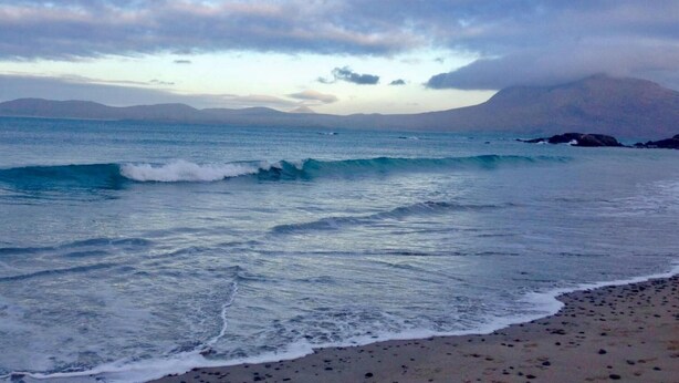 Una spiaggia con onde, cielo sereno e montagne in lontananza.