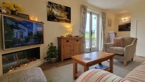 Ein gemütliches Wohnzimmer mit Kamin, Fernseher, Sofa, Sessel und Esstisch.
