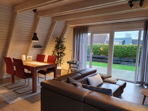 A modern loft-style living space with a dining area, a sofa, and a large window offering a view of the backyard.