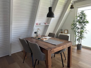 A dining area with a wooden table, grey upholstered chairs, a hanging pendant light, and a potted plant.