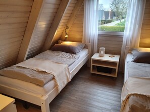 A cozy attic bedroom with two single beds, a small bedside table, and a window with curtains.