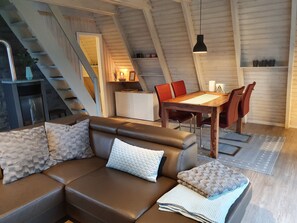 A cozy living area with a brown leather sofa, a wooden dining table with red chairs, and a staircase leading to an upper level.