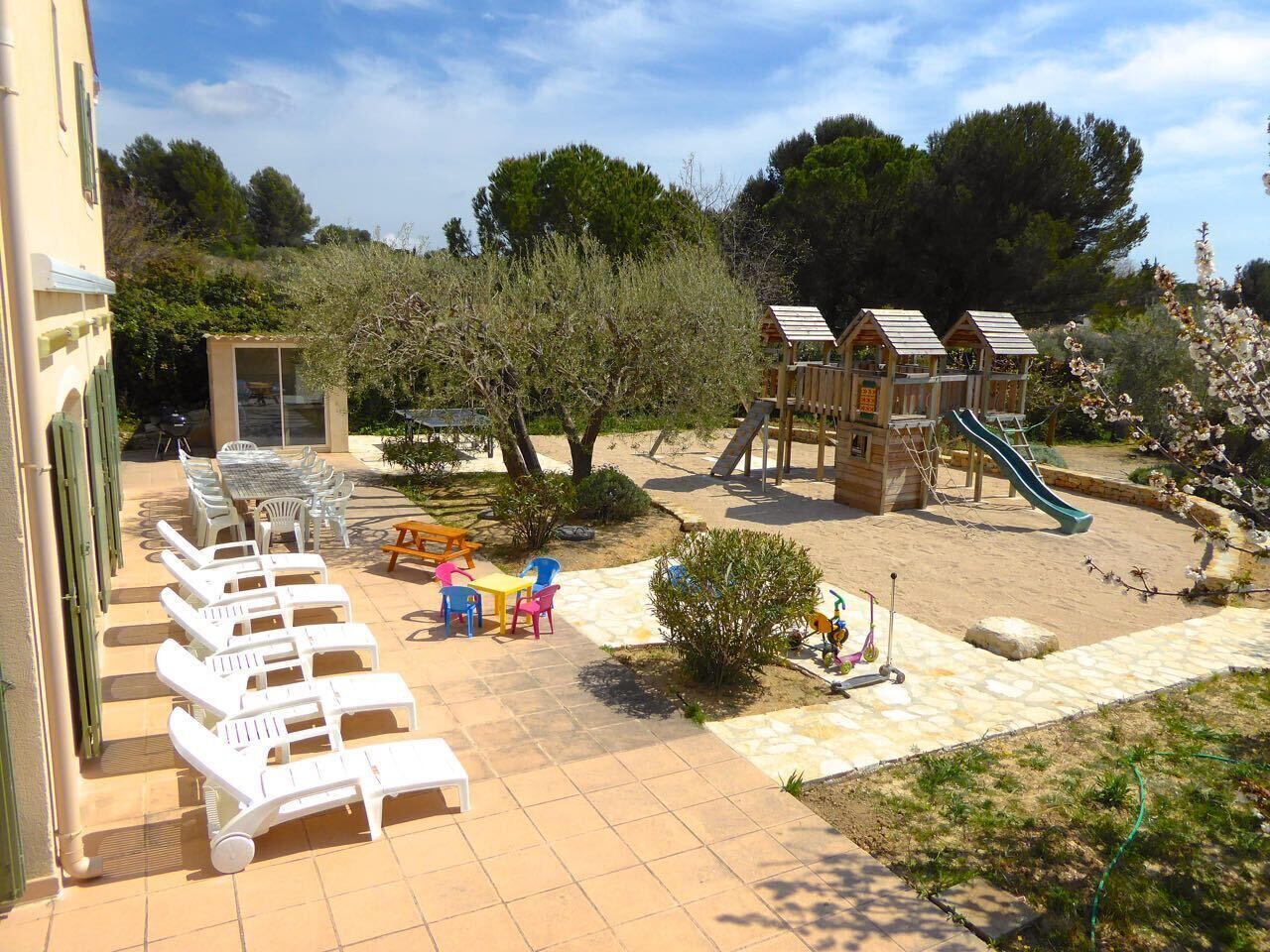 Un espacio exterior soleado con sillones, un pequeño parque infantil y un tobogán.