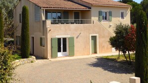 A two-story house with a tiled roof, a balcony, and a paved driveway.