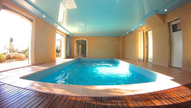 An indoor swimming pool with wooden decking, surrounded by walls and doors.