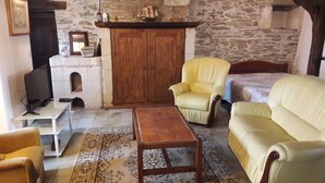 Una sala de estar acogedora con una pared de piedra, un mueble de madera, un televisor, una alfombra estampada y dos sofás color crema.