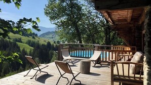 Une terrasse en bois avec des chaises longues donnant sur une piscine et sur des collines pittoresques.