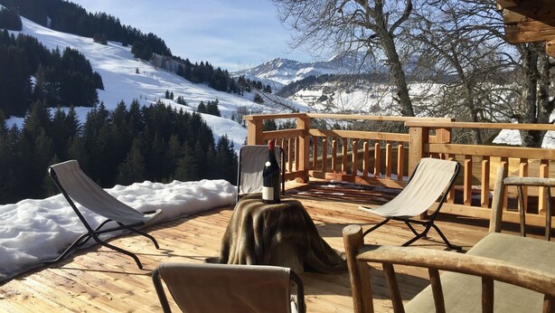 Une terrasse en bois avec des chaises longues donnant sur un paysage montagneux enneigé.