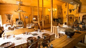 Un intérieur rustique en bois, avec un coin repas aménagé pour quatre personnes, comprenant une table avec couverts et verres, ainsi qu’un banc décoré d’un pommeau de pin.