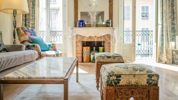 Ein Wohnzimmer mit Sofa, Glastisch, gestreiftem Hocker, Kamin und Blick auf den Balkon.