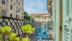 Ein Balkon mit schmiedeeisernem Geländer, einem kleinen Tisch mit Stühlen und Blumentöpfen.