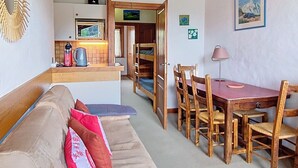Een knus woongedeelte met een kitchenette, een eethoek met houten meubels en een bank met kussens.