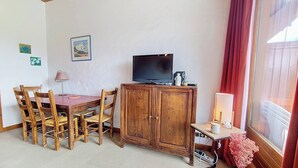 Een kamer met een houten eettafel en stoelen, een kast met een televisie, en een raam met gordijnen.