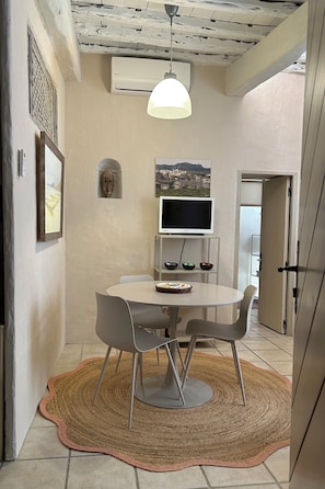A dining area with a round table, chairs, a woven rug, a wall-mounted TV, and a ceiling fan. - IN THE HEART OF THE HISTORIC DISTRICT: ALL THE CHARM OF BONIFACIO IN A SPACIOUS 2+1 STUDIO (Bonifacio)