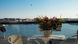 A table with a potted plant and a chair on a balcony overlooking a body of water with a cityscape in the background. - Luxury 4* apartment with closed garage and pond view 50m from the Sillon beach (Saint-Malo)