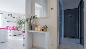 A modern living room with a white console table, a mirror, and a potted plant. - Luxury 4* apartment with closed garage and pond view 50m from the Sillon beach (Saint-Malo)