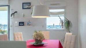 A dining area with a red table, white chairs, a vase of flowers, and a city view through the window. - Luxury 4* apartment with closed garage and pond view 50m from the Sillon beach (Saint-Malo)