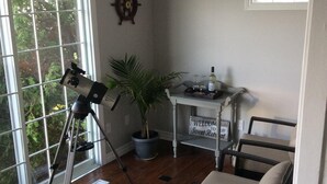 A room with a telescope, a potted plant, wicker furniture, and a welcome sign.